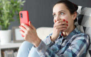 Brunette White Woman Gasps and covers her mouthas she holds a red phone