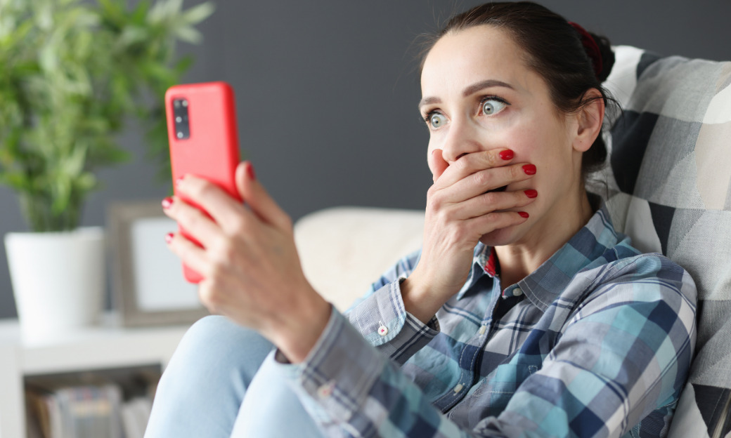 Brunette White Woman Gasps and covers her mouthas she holds a red phone